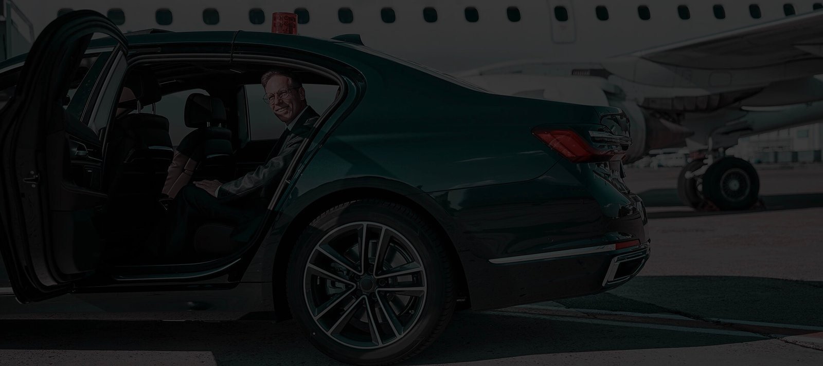 A chauffeur opening the rear door for a passenger beside a private jet